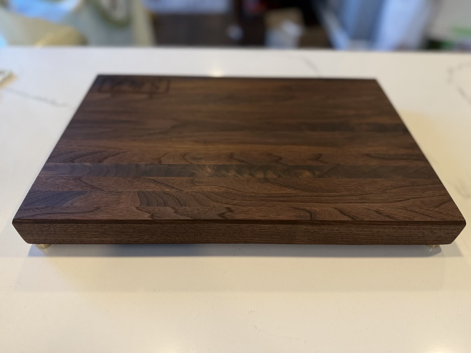 A walnut edge-grain board with brass feet and an engraved mark in one corner