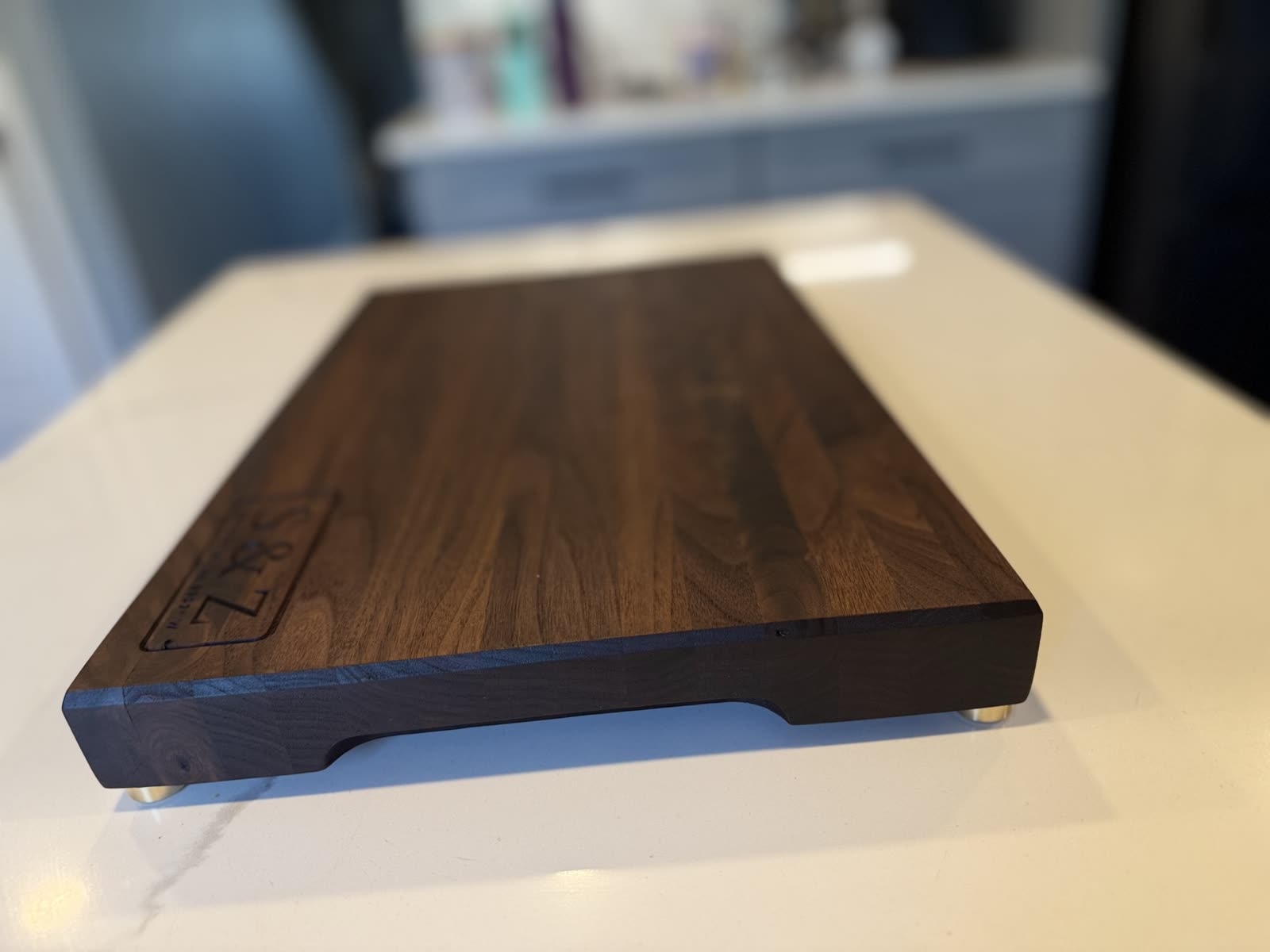 A walnut serving board with brass feet and a monogram carved in one corner