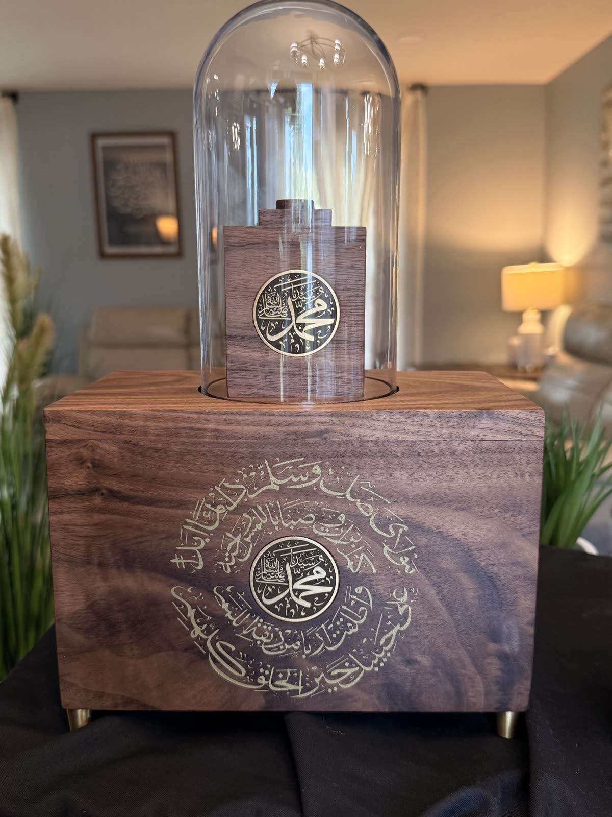 A walnut relic display case with a glass dome, a gold-filled calligraphy medallion and brass feet, in a living room