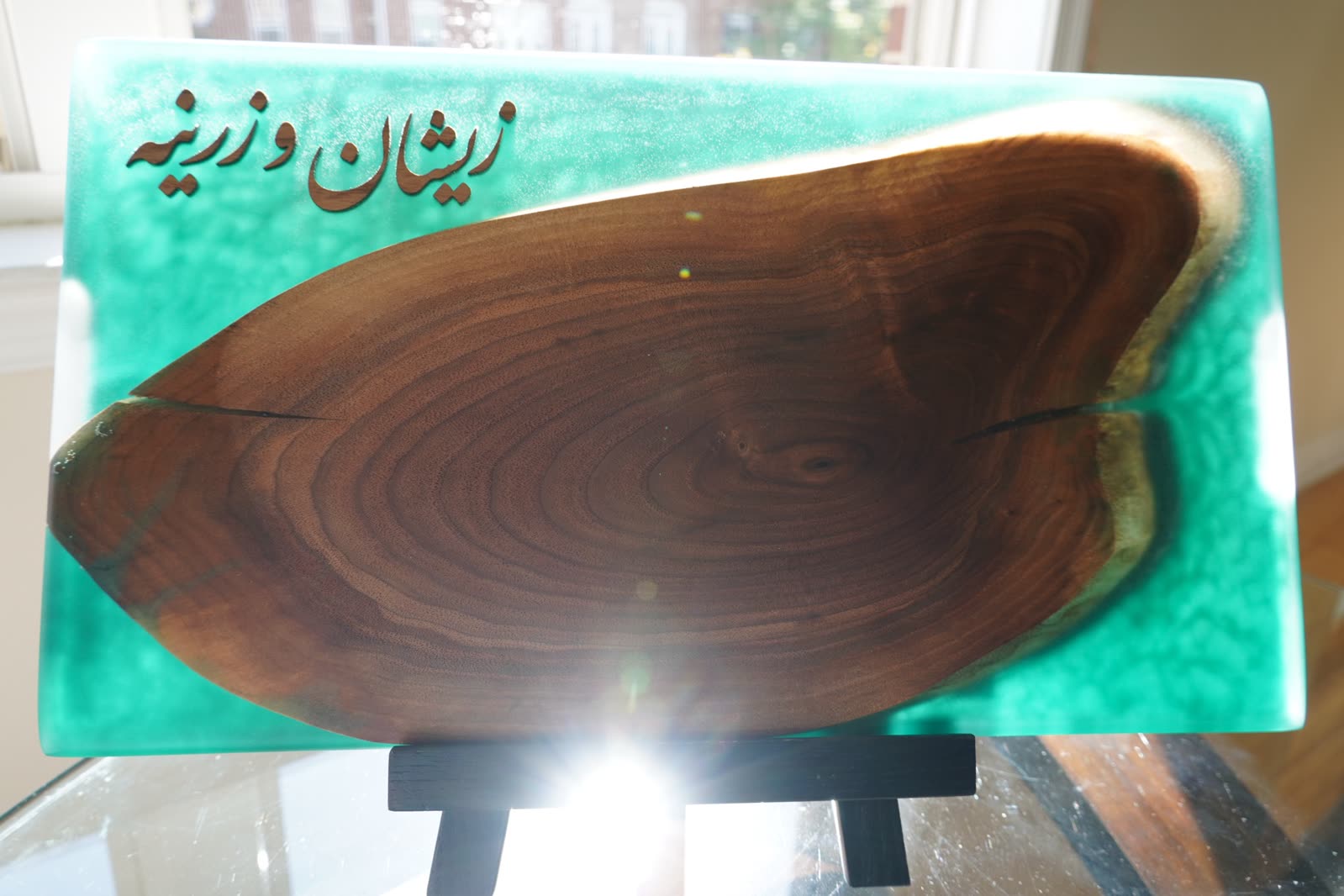 A walnut cross-section set in emerald resin with a name carved in Arabic script, on a small stand